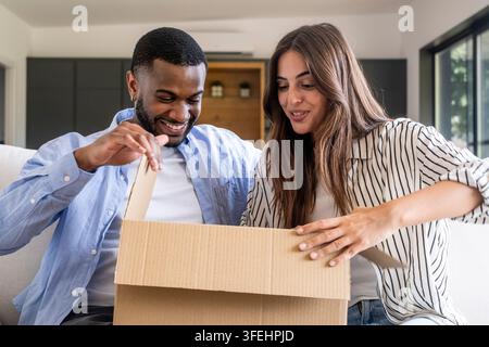 Coppia felice che disimballa una scatola di cartone a casa, sorridendo mentre aprono una consegna e condividono un momento gioioso insieme Foto Stock