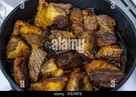 Primo piano dall'alto cattura pezzi di manzo succulenti che cuociono a fuoco lento in un liquido scuro. La texture ricca e il calore evocano un'esperienza culinaria sostanziosa. Foto Stock
