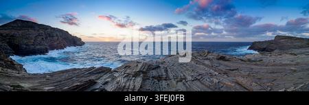 Stintino, Sardegna, Italia. Vista panoramica di una drammatica costa frastagliata con onde che si infrangono contro le scogliere durante il tramonto Foto Stock
