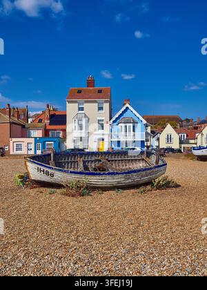 Barche da pesca consumate sulla spiaggia di ciottoli della città costiera di Aldeburgh con case costiere storiche e colorate Foto Stock