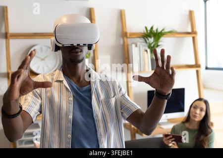 Diversi colleghi che testano un visore VR in ufficio a casa, uomo che raggiunge con una camicia a righe, donna che osserva Foto Stock