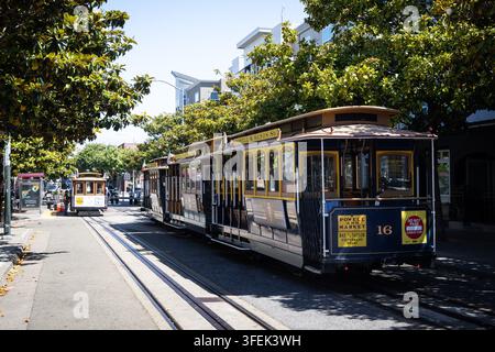 SAN FRANCISCO, USA - 3 LUGLIO 2026: Un tram storico Powell and Market si muove lungo i binari di Taylor Street a Fishermans Wharf, incorniciato da alberi maturi Foto Stock