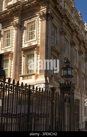 La luce del sole illumina l'edificio di HM Treasury dietro le cancellate di sicurezza all'angolo tra Whitehall e Downing Street a Westminster. Foto Stock