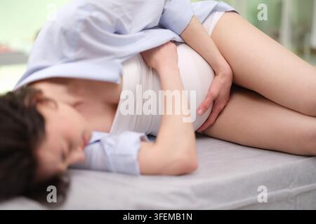 Donna incinta con dolori addominali sdraiata su un divano nel reparto di ginecologia dell'ospedale Foto Stock