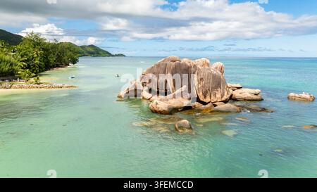 Enormi massi di granito si trovano in acque turchesi calme vicino alla lussureggiante costa. Praslin, Seychelles. Foto Stock