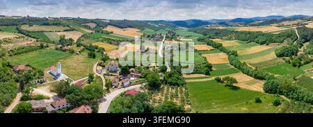 Veduta aerea che cattura un pacifico villaggio rurale con case, chiesa, strade e campi agricoli circondati da dolci colline verdi Foto Stock