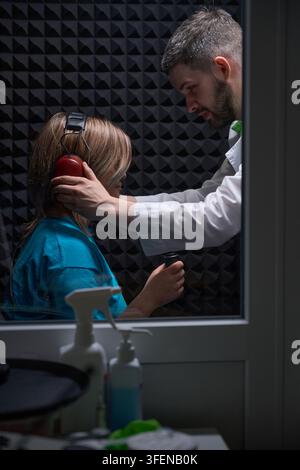 Giovane donna che si sottopone a un test uditivo con un medico in una cabina insonorizzata Foto Stock