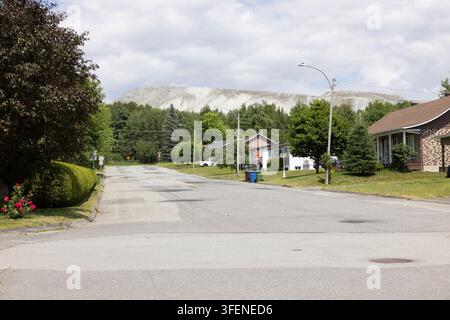 Canada, Thetford Mines, 11-07-2025. Una strada residenziale a Thetford Mines con un enorme cumulo di scorie minerarie di amianto che si erge direttamente dietro le case Foto Stock