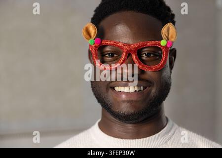 Uomo afroamericano che sorride indossando occhiali novelty con glitter rossi e un maglione color crema in studio Foto Stock