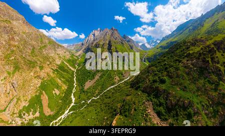 Vista panoramica di una maestosa catena montuosa con picchi rocciosi e pendici verdi. Un fiume serpeggiante scorre attraverso la valle sotto un cielo sereno. Foto Stock