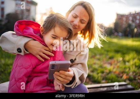 Madre e figlia si legano all'aperto, guardando lo smartphone Foto Stock