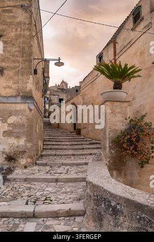 Stretta strada acciottolata con scale in pietra al tramonto a Matera, Italia Foto Stock