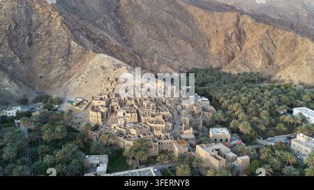 Vista aerea delle antiche rovine in mattoni di fango di Birkat Al Mouz circondate da una lussureggiante oasi di palme da dattero e da un paesaggio montuoso aspro a Birkat Al Mouz, Ad Foto Stock