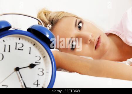 Insonnia con orologio di notte. Giovane donna bionda che non riesce a dormire, la sveglia segna le 2:25 di notte, foto in studio, Repubblica Federale di Germania Foto Stock