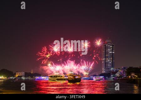 Vista dei fuochi d'artificio sul fiume Chao Phraya vicino al Memorial Bridge con barche fluviali illuminate e lo skyline della città di notte a Bangkok, Bangkok, Thailandia Foto Stock