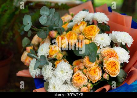 Un bouquet vivace legato a mano con rose arancioni e rose spray, crisantemi bianchi, foglie di eucalipto e piccoli boccioli color pesca. I fiori Foto Stock