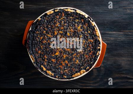 Torta di mirtilli fatta in casa appena sfornata su sfondo di legno scuro, vista dall'alto, primo piano. Deliziosa torta di mirtilli intera appena sfornata in stampo di ceramica Foto Stock