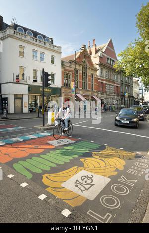 Un ciclista attraversa un passaggio pedonale dipinto a banana a Fulham Broadway Foto Stock