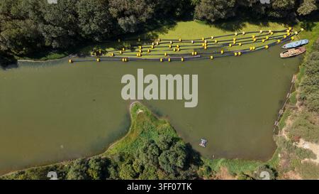 Vista aerea del fiume Tamis con una barriera galleggiante per detriti dotata di boe gialle, piccole barche ormeggiate vicino alla riva e alberi rigogliosi lungo il fiume Foto Stock