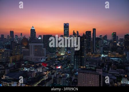 Vista aerea dei grattacieli di Bangkok illuminati contro un cielo vibrante al tramonto con architettura moderna e densità urbana a Bangkok, Thailandia. Foto Stock