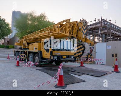 Camion gru mobile giallo parcheggiato all'interno della zona di sicurezza durante i lavori di manutenzione al Museo Nazionale del Qatar. Foto Stock