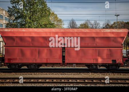 Un vagone ad alta cassa europeo rosso per il trasporto di materiali sfusi come ghiaia e minerali, posizionato sui binari ferroviari sotto le linee aeree di contatto, con Foto Stock
