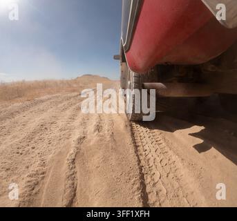 Tracce di pneumatici nella sabbia, camion rosso, erba secca, cielo sereno Foto Stock