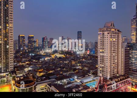 Vista ad angolo alto della skyline di Jakarta al crepuscolo, che mostra grattacieli moderni illuminati in contrasto con densi quartieri urbani sotto un cielo al crepuscolo. Foto Stock