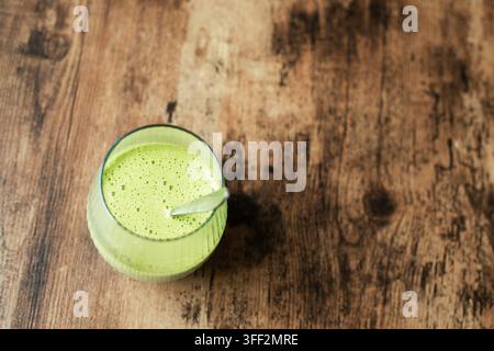 Latte matcha verde o frullato sano in un bicchiere a costolature con un cucchiaio su un tavolo di legno Foto Stock