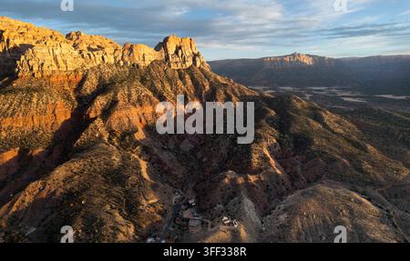 Vista aerea del parco nazionale di Zion, Utah, mentre un'alba dorata illumina le imponenti scogliere di arenaria e il paesaggio desertico accidentato. Foto Stock