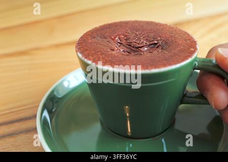Prima piano della mano di un uomo che tiene una tazza verde di caffè Marocchino espresso caldo Foto Stock