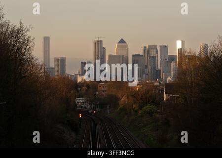 La luce dell'ora dorata si riflette sullo skyline di Canary Wharf a Londra (One Canada Square) dai binari ferroviari vicino alla stazione di Canary Wharf. Foto Stock