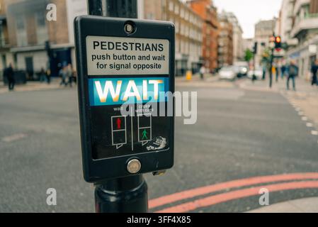 Prima piano di un pulsante per passaggio pedonale britannico con segnale di ATTESA illuminato, una caratteristica familiare delle strade di Londra - Londra, Regno Unito - 2 Foto Stock