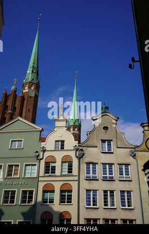 Facciate storiche di case colorate sotto alte guglie verdi di chiese contro un cielo blu terso nella zona della vecchia città di Danzica, Polonia. Foto Stock