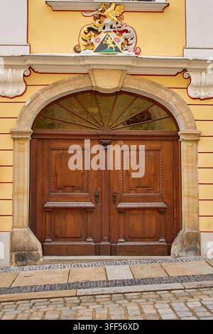 Grande porta doppia in legno con finestra ad arco e stemma decorativo sulla facciata dell'edificio. Architettura storica e dettaglio architettonico Foto Stock