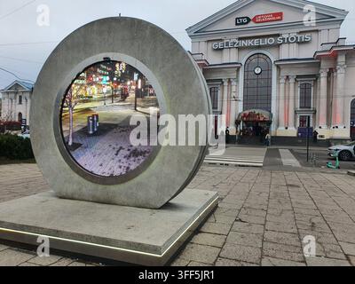 Una grande scultura circolare in cemento con uno schermo digitale che mostra una scena urbana notturna si trova su una piazza lastricata davanti a Vilnius Foto Stock