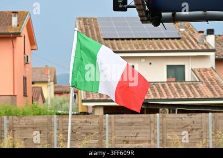 Bandiera tricolore italiana su un palo sopra case con pannelli solari installati sul tetto Foto Stock