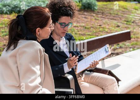Donne d'affari che hanno un incontro all'aperto e rivedono un documento su una clipboard Foto Stock