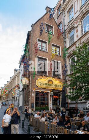 Bruxelles, Belgio - 25 agosto 2026: Vivace caffè all'aperto su una stretta strada cittadina a Bruxelles, con decorazioni colorate di biciclette che scalano un alto mattone Foto Stock