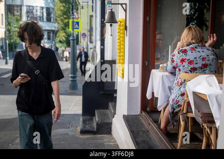 Mosca, Russia, 1 settembre 2026, Persona che utilizza un telefono cellulare mentre passa davanti a un tavolo da caffè all'aperto Foto Stock