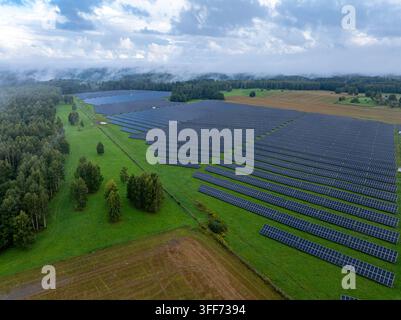 Vista aerea di una grande centrale solare con pannelli fotovoltaici circondata da foresta e campagna Foto Stock