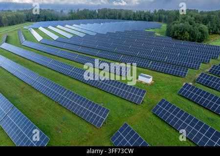 Vista aerea con drone di una fattoria solare con pannelli fotovoltaici e foresta verde nella campagna rurale Foto Stock