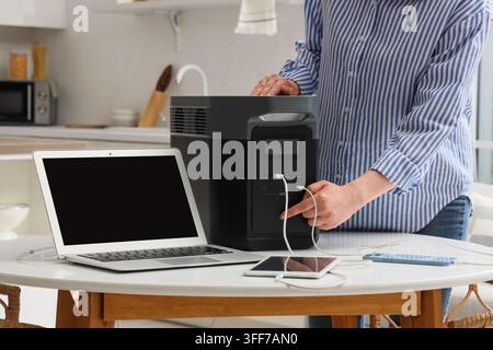 Indipendenza energetica e alimentazione di emergenza, persona che ricarica laptop e dispositivi mobili con una stazione di potenza portatile a casa durante un blackout o un'interruzione Foto Stock