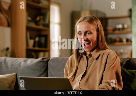 Giovane donna caucasica entusiasta che guarda lo schermo del laptop durante gli acquisti online del Black Friday. Immagine adatta al marketing digitale, alla vendita e-commerce Foto Stock