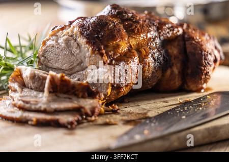 Gustoso collo di maiale arrosto con una crosta croccante è guarnito con rosmarino fresco e affettato su una tavola di legno. Questo scatto culinario professionale si adatterà pe Foto Stock
