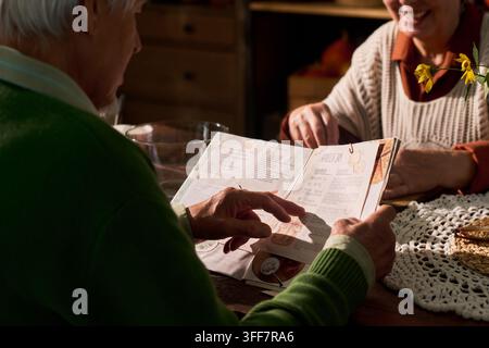 Coppia di anziani che legge insieme un libro di ricette a tavola Foto Stock