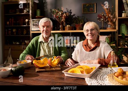 Ritratto di una coppia di anziani che prepara fette di zucca per la cottura al forno Foto Stock