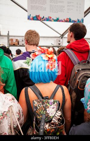 RAGAZZA DEL FESTIVAL CON CAPELLI BLU VISTA DA DIETRO, REPORTAGE, GREEN MAN FESTIVAL 2013, BRECON, GALLES, REGNO UNITO, 2013: Visto da dietro, una partecipante al festival con capelli blu brillanti decorati con fiori rossi e bianchi si trova in una folla al Courtyard Bar portando uno zaino a fantasia. Foto: Rob Watkins. INFO: Il Green Man Festival si tiene ogni anno ad agosto nelle Brecon Beacons. Celebra la musica alternativa, le arti, la letteratura, la scienza e una cultura a misura di famiglia in uno splendido scenario montano. L'evento del 2013 è stato l'edizione del 10° anniversario. Foto Stock