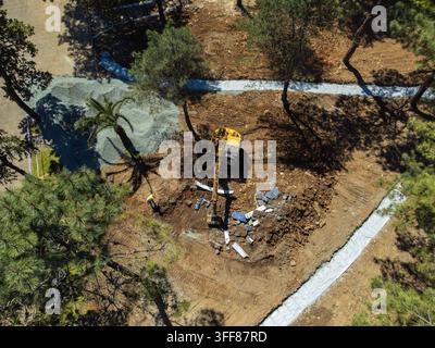 Attrezzature per lo spostamento della terra che lavorano in un cantiere edile, preparando il terreno per un nuovo sviluppo mentre i lavoratori sono presenti, visti da una vista aerea sur Foto Stock