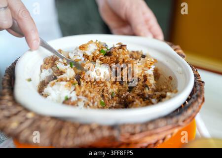 Una vista ravvicinata mostra riso bianco con salsa marrone e guarnizione verde mescolati in una ciotola bianca con un cucchiaio. Foto Stock